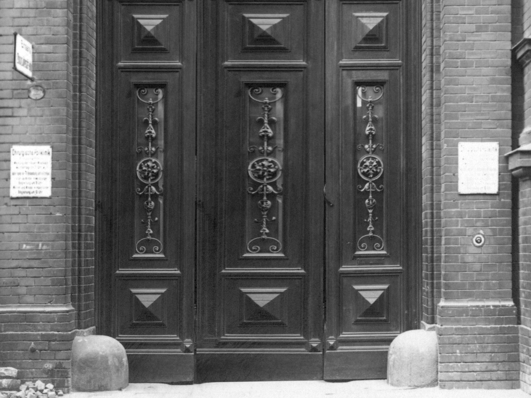 Fotografie, schwarz-weiß, vermutlich aus den 1920er Jahren. Das Foto zeigt das Portal zur chirurgischen Poliklinik der Charité. Die schwere Holztür steht offen. 