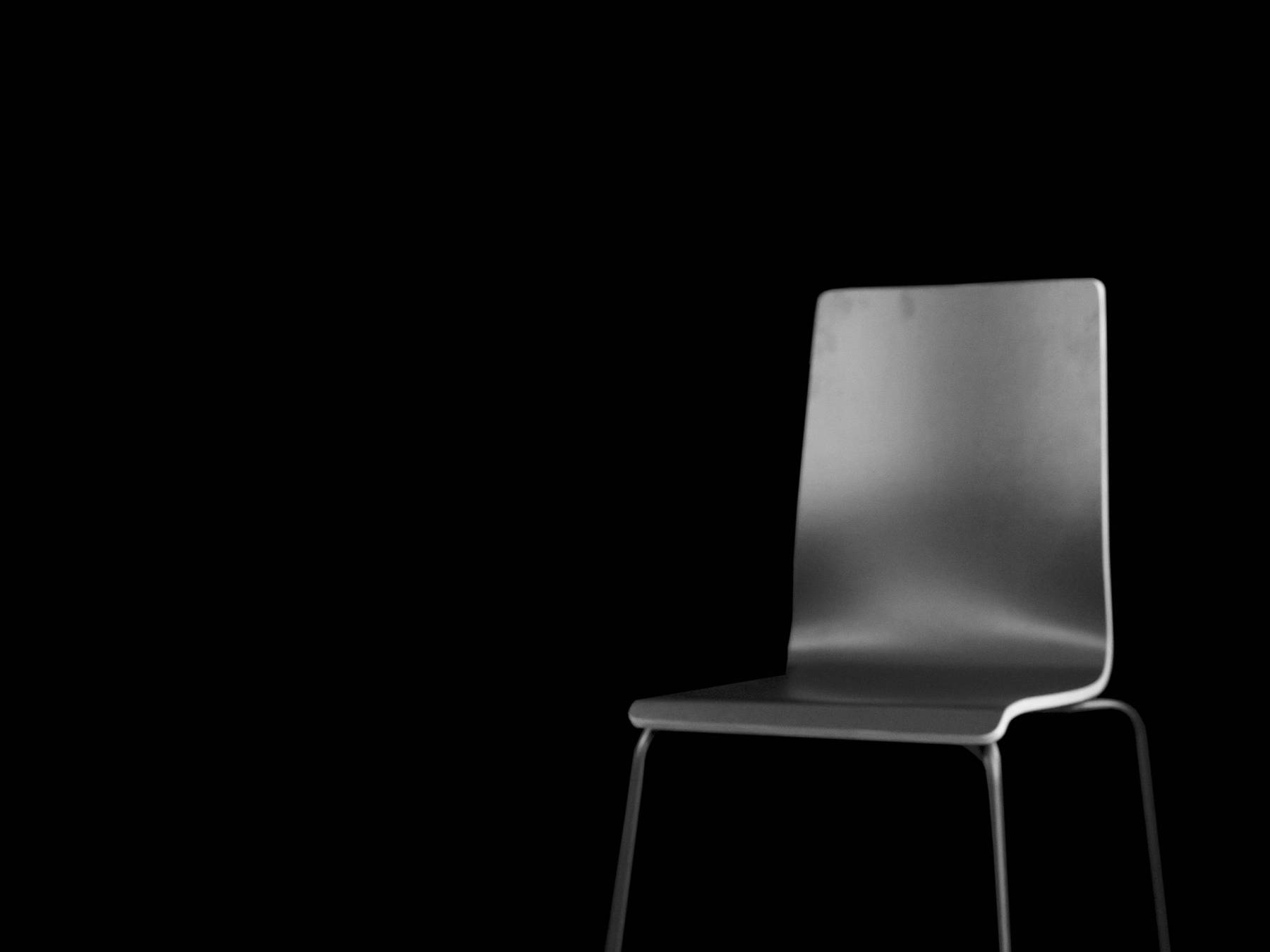 Fotografie, schwarz-weiß, von 2022: Das Foto zeigt einen leeren schwarzen Raum. Im Vordergrund sieht man links ein Mikrophon zur Tonaufnahme und rechts einen leeren Stuhl. 